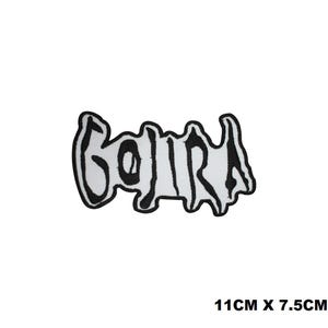 Op de afbeelding: Een geborduurde patch met het woord GOJIRA in een gestileerd, grillig zwart lettertype op een witte achtergrond. De patch heeft een zwarte rand en meet 11 cm bij 7,5 cm. Het ontwerp is plat en heeft een gedurfde, grafische uitstraling.