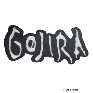 以下が含まれることがあります： 黒い刺繍ワッペンで、白い文字で「GOJIRA」とスタイリッシュでギザギザしたフォントで書かれています。ワッペンには黒い縁取りがあり、画像右下の印刷されたテキストが示す通り、サイズは11cm x 7.5cmです。