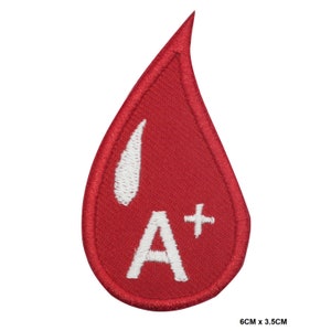 May include: Red blood drop shaped iron-on patch with white embroidered text "A+" and a white drop inside the blood drop. The patch measures 6 cm by 3.5 cm.