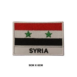 May include: An embroidered patch featuring the flag of Syria. The patch is white with a red, white, black, and green flag in the centre. The flag has two green stars. The words "SYRIA" are printed in black below the flag. The patch measures 9 cm by 6 cm.