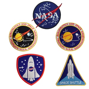 May include: Five embroidered patches featuring NASA logos. The patches are circular, shield-shaped, and triangular. The patches feature the NASA logo, the words "National Aeronautics and Space Administration", and the words "Space Shuttle".
