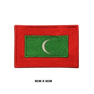 May include: A red and green embroidered patch featuring the flag of the Maldives. The flag has a white crescent moon on a green background, surrounded by a red border. The patch measures 9 cm by 6 cm.