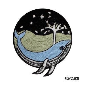 Peut inclure: Écusson brodé rond représentant une baleine bleue sous un ciel étoilé. L'écusson a un fond noir avec un paysage vert clair. La baleine est bleu clair. Dimensions : 8 cm x 9 cm.