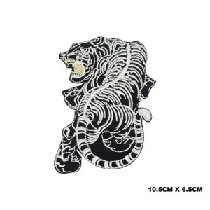 May include: Embroidered patch of a black tiger with white detailing, including the tiger's stripes and facial features. The patch measures 10.5cm by 6.5cm. The tiger is depicted in a dynamic pose, with its mouth open.