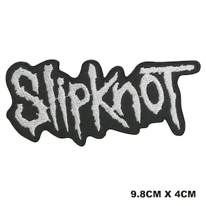 May include: An embroidered patch featuring the word Slipknot in a jagged, white, stylized font against a black background. The patch has an irregular, die-cut border that follows the shape of the lettering. It measures 9.8 cm by 4 cm.