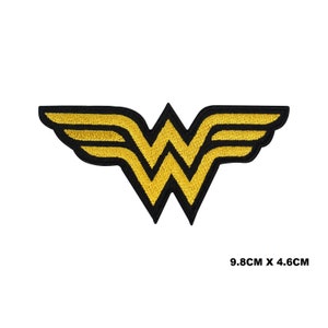 May include: A gold Wonder Woman logo with a black outline. The logo is 9.8 cm by 4.6 cm.