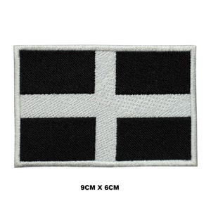 May include: A white and black embroidered patch with a white cross on a black background. The patch measures 9cm by 6cm.