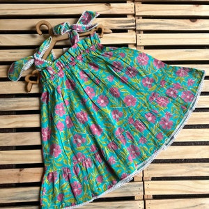 May include: A turquoise blue dress with a pink floral print and white lace trim. The dress has a gathered bodice and a tiered skirt.