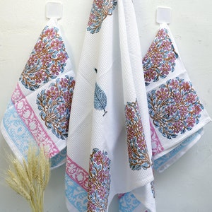 Puede incluir: Tres toallas de cocina blancas con un patrón floral azul y rosa. Las toallas están colgadas de ganchos en una pared blanca.