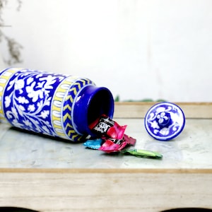 Peut inclure: Un pot en céramique bleu et blanc avec un motif floral et des accents jaunes. Le couvercle est ouvert et des bonbons colorés se répandent du pot.