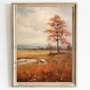 May include: A framed painting of a landscape with a single tree in the foreground. The tree has orange and red leaves and is set against a backdrop of a field and distant hills. The sky is a soft blue with white clouds.