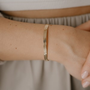 Könnte beinhalten: Ein dünnes, schlangenförmiges Armband in Goldtönen am Handgelenk einer Person.