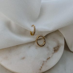 Puede incluir: Dos pendientes de aro dorados con una fila de pequeñas piedras transparentes alrededor del borde.