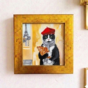 Op de afbeelding: Een ingelijst schilderij van een zwart-witte kat met een rode baret en sjaal, die een croissant vasthoudt. De Eiffeltoren is zichtbaar op de achtergrond. Het schilderij zit in een gouden lijst.