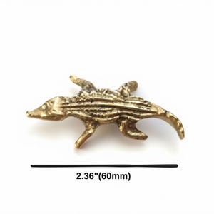 K&ouml;nnte beinhalten: Eine messingfarbene Metall-Alligatorfigur mit strukturiertem, geschupptem R&uuml;cken und vier Beinen. Die Figur misst 60 mm in der L&auml;nge, wie durch den Text darunter angegeben. Das Objekt hat eine metallische Oberfl&auml;che und eine detaillierte Form.