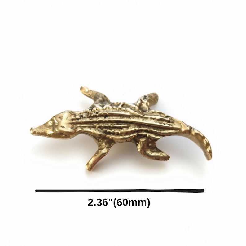 K&ouml;nnte beinhalten: Eine messingfarbene Metall-Alligatorfigur mit strukturiertem, geschupptem R&uuml;cken und vier Beinen. Die Figur misst 60 mm in der L&auml;nge, wie durch den Text darunter angegeben. Das Objekt hat eine metallische Oberfl&auml;che und eine detaillierte Form.