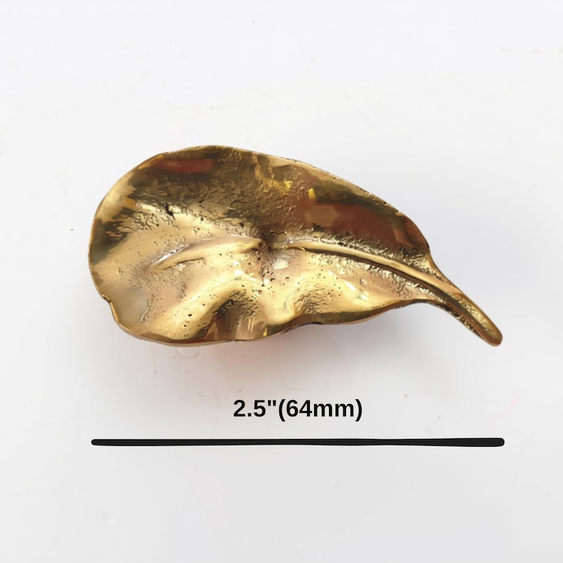 K&ouml;nnte beinhalten: Ein metallisch goldfarbenes, blattf&ouml;rmiges Objekt mit strukturierter Oberfl&auml;che und einer zentralen Blattader. Das Objekt befindet sich &uuml;ber einer schwarzen Linie und einem Text, der eine L&auml;nge von 64 mm bzw. 2,5 Zoll angibt.