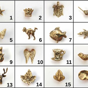 K&ouml;nnte beinhalten: Eine Sammlung von sechzehn kleinen, goldfarbenen Metallanh&auml;ngern in einem Raster, die verschiedene Formen wie einen Seestern, eine Krone, eine Schildkr&ouml;te, V&ouml;gel, einen Schmetterling, eine Katze, einen Fisch, einen Alligator, Fl&uuml;gel, eine Teetasse, einen Hirschkopf und verschiedene Bl&auml;tter zeigen, jeweils nummeriert von 1 bis 16.