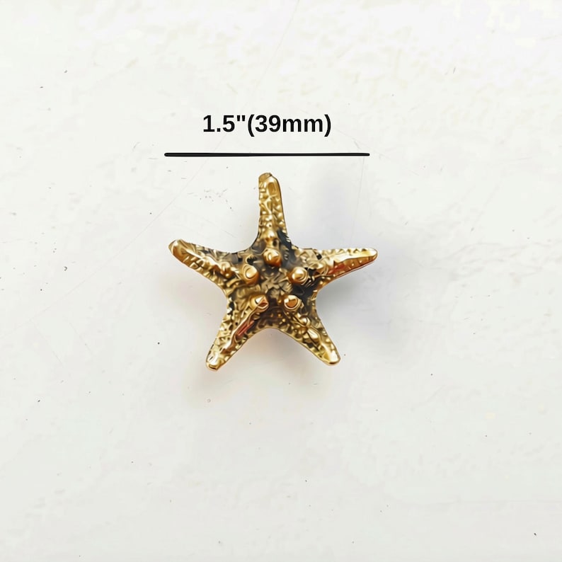 K&ouml;nnte beinhalten: Ein goldfarbener Seestern-Anh&auml;nger mit strukturierter, noppiger Oberfl&auml;che und f&uuml;nf Armen. Das Objekt ist mit einer Gr&ouml;&szlig;enangabe von 39 mm versehen. Das Finish weist dunkle, vertiefte Bereiche auf, die die detaillierte Textur betonen.