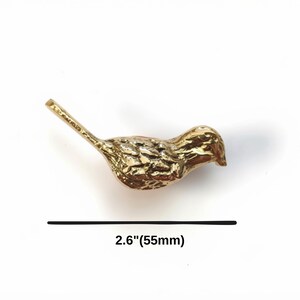 K&ouml;nnte beinhalten: Eine goldfarbene Metallvogel-Figur mit einem strukturierten Federmuster auf dem K&ouml;rper und einem langen Schwanz. Der Vogel ist &uuml;ber einer schwarzen horizontalen Linie positioniert, unter der der Text 2.6"(55mm) steht, was eine L&auml;nge von 55 mm angibt.