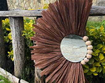May include: A brown paper mache sunburst mirror with a round mirror in the center and wooden beads around the edge.