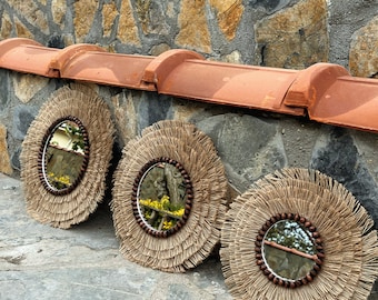 May include: Three round mirrors with brown wooden frames and natural fiber fringe. The mirrors are hanging on a stone wall with a terracotta tile roof.