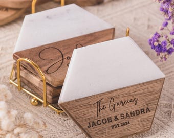 May include: Hexagonal coasters with a gold-coloured metal holder. Each coaster combines white marble with a wooden base. The wooden section is engraved with a name and date. A stylish home decor item.