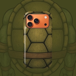 May include: A phone case featuring a turtle shell design with an orange camera module. The case has a textured, olive green pattern with a brown band. The background shows a cartoon turtle.
