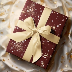 Puede incluir: Una caja de regalo color burdeos con una cinta dorada y un dise&ntilde;o navide&ntilde;o con copos de nieve, estrellas y &aacute;rboles. La caja est&aacute; envuelta en papel festivo y se encuentra sobre un fondo blanco con purpurina dorada.