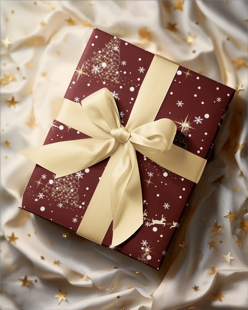Puede incluir: Una caja de regalo color burdeos con una cinta dorada y un dise&ntilde;o navide&ntilde;o con copos de nieve, estrellas y &aacute;rboles. La caja est&aacute; envuelta en papel festivo y se encuentra sobre un fondo blanco con purpurina dorada.
