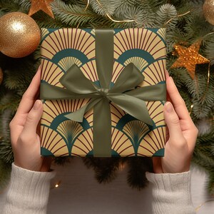 May include: A green, yellow, and red gift box with a green ribbon is being held by two hands. The box is wrapped in a patterned paper with a geometric design. The box is surrounded by a Christmas tree with gold ornaments and stars.