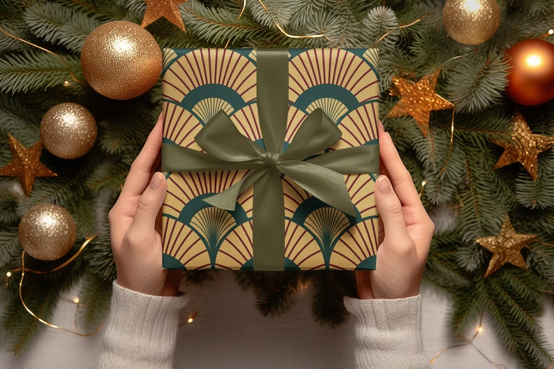 May include: A green, yellow, and red gift box with a green ribbon is being held by two hands. The box is wrapped in a patterned paper with a geometric design. The box is surrounded by a Christmas tree with gold ornaments and stars.