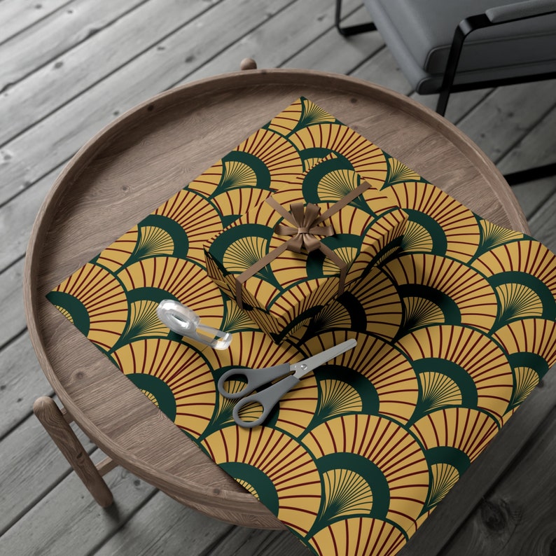 May include: Gold and green patterned gift wrap with a red accent. The wrap features a repeating design of stylised fans. A brown ribbon is tied around a gift box on top of the wrap.