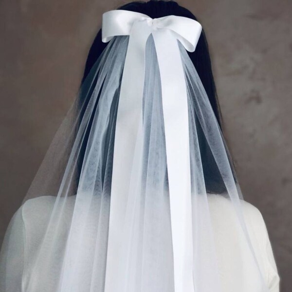 A veil bow in one layer of soft tulle with a satin bow made of satin ribbon is attached to the hairpin in the hair.