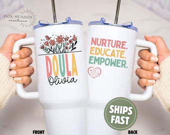 Puede incluir: Vaso térmico blanco con asa. La parte delantera muestra la palabra "DOULA" en letras coloridas, un diseño floral y el nombre "Olivia". La parte trasera tiene las palabras "NURTURE. EDUCATE. EMPOWER." y un corazón con un bebé.