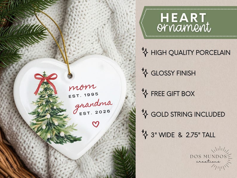 May include: A white heart-shaped porcelain ornament with a glossy finish, featuring a green Christmas tree illustration with a red bow, and the text "mom EST. 1995" and "grandma EST. 2026" with a small red heart. It includes a gold string and measures 3" wide by 2.75" tall.