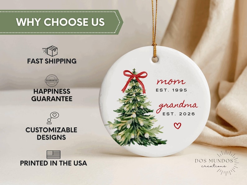 May include: A round white ceramic ornament hanging from a gold string. It features a watercolor green Christmas tree with a red bow on top. The text reads mom EST. 1995 and grandma EST. 2026 in red and black, with a small red heart below the text.