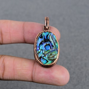 Op de afbeelding: Ovaalvormige hanger met een koperen frame en een iriserende abalone schelp inlay. De schelp heeft tinten blauw, groen en paars.