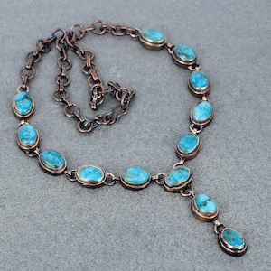 May include: A copper chain necklace with oval turquoise stones. The necklace has a Y-shaped pendant with a larger turquoise stone.