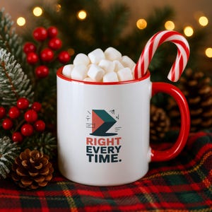 May include: A white ceramic mug with a red rim and handle, filled with white marshmallows and a red and white striped candy cane. The mug features a geometric logo and the text RIGHT EVERY TIME. printed in dark blue and red on the front side.