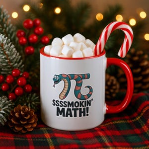 Op de afbeelding: Een witte keramische mok met een rode rand en handvat, gevuld met witte marshmallows en een rood-witte zuurstok. De mok is voorzien van een getekende slang in de vorm van het pi-symbool en de zwarte tekst SSSSMOKIN' MATH! op de voorzijde.