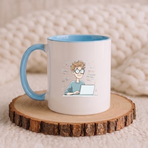 Può includere: Una tazza in ceramica bianca con interno e manico azzurro, caratterizzata da un'illustrazione a cartone animato di una persona con capelli castani ricci e occhiali che lavora al computer portatile, circondata da piccole forme e linee astratte.