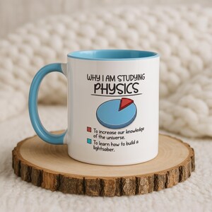 May include: A white ceramic mug with a light blue handle and interior rim. The mug features the text "WHY I AM STUDYING PHYSICS" above a pie chart. The chart includes a red slice labeled "To increase our knowledge of the universe" and a blue slice labeled "To learn how to build a lightsaber."