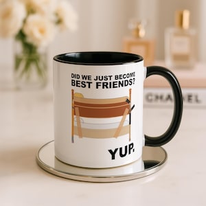 Può includere: Una tazza in ceramica bianca con interno e manico neri, caratterizzata da un grafico di un letto a castello in legno. Il testo sopra il letto recita DID WE JUST BECOME BEST FRIENDS? e la parola YUP. è stampata in nero sotto l'illustrazione.