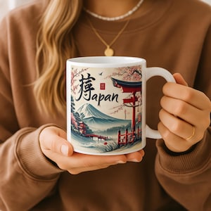 May include: White ceramic mug featuring a Japanese landscape design with a mountain, red torii gate, and cherry blossoms. The mug has the word "Japan" in both Japanese characters and English.