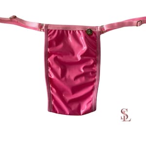 May include: A bright pink thong with a shiny, wet-look finish. The garment has thin, adjustable straps and a small gold-colored charm. The edges are trimmed with a lighter pink material. The logo "$L" is in the lower right corner.