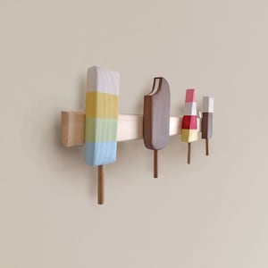 May include: Wooden popsicle shaped wall hooks in various colors, including yellow, blue, red, white, and brown. The hooks are mounted on a wooden bar.