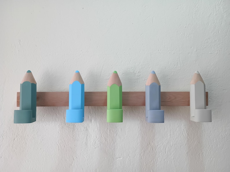 May include: Five wooden pencil-shaped coat hooks in different colors: light blue, green, gray, light blue, and gray. The hooks are mounted on a wooden board.