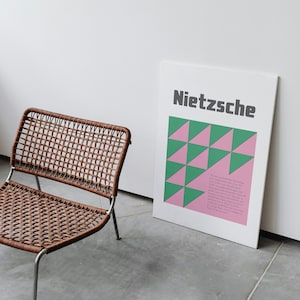 May include: A brown wicker chair with a silver metal frame sits in front of a white wall with a poster that reads "Nietzsche" in black text. The poster has a geometric pattern of pink and green triangles.