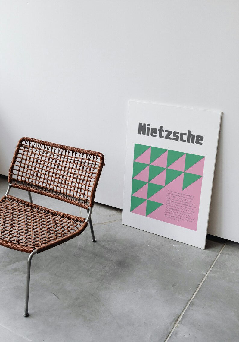 May include: A brown wicker chair with a silver metal frame sits in front of a white wall with a poster that reads "Nietzsche" in black text. The poster has a geometric pattern of pink and green triangles.